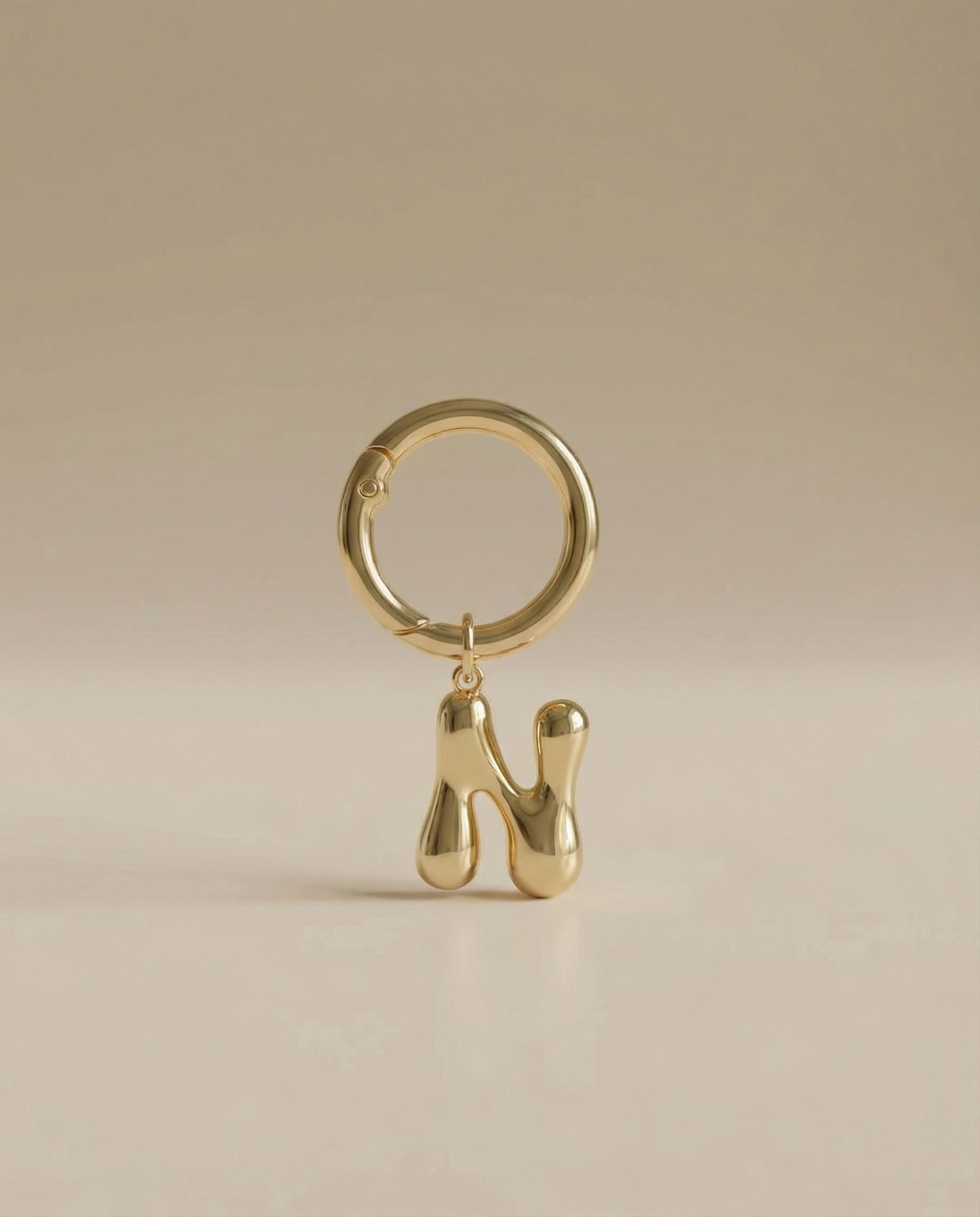 Gold charm in the letter 'N' attached to a gold keyring on beige background