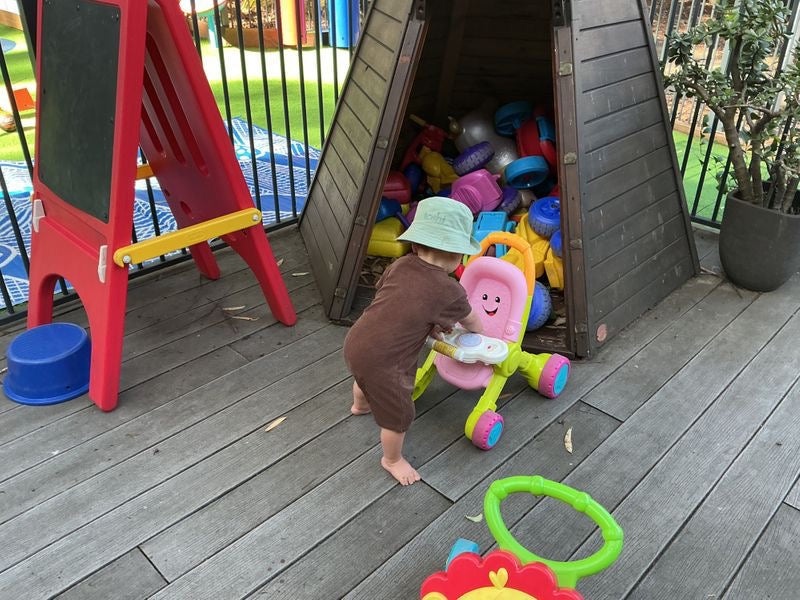 Child playing with toys near a playhouse on a wooden deck at daycare