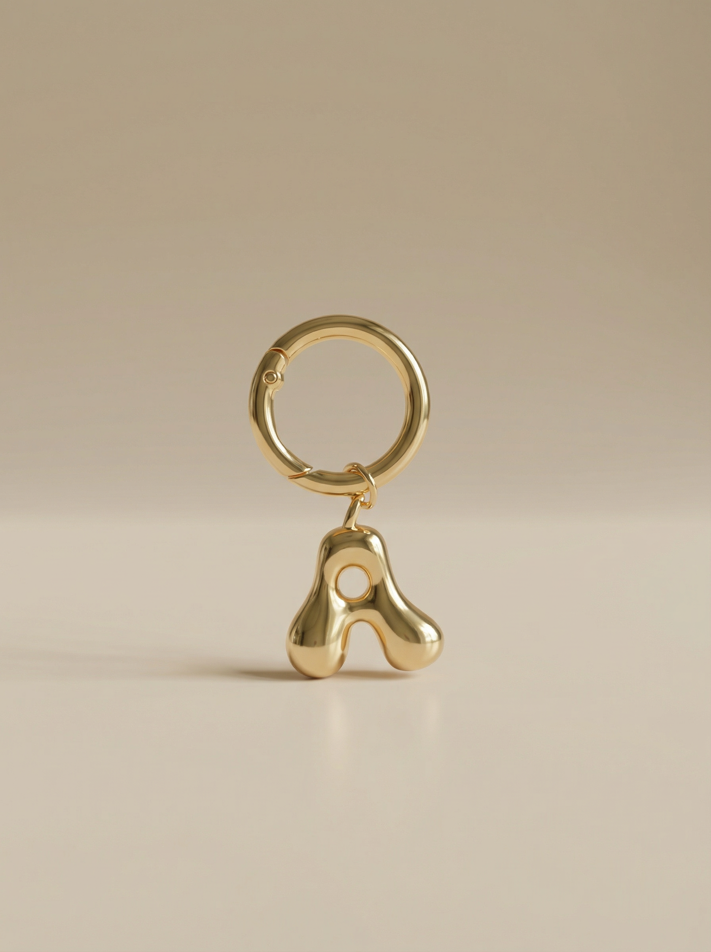 Gold charm in the letter 'A' attached to a gold keyring on beige background