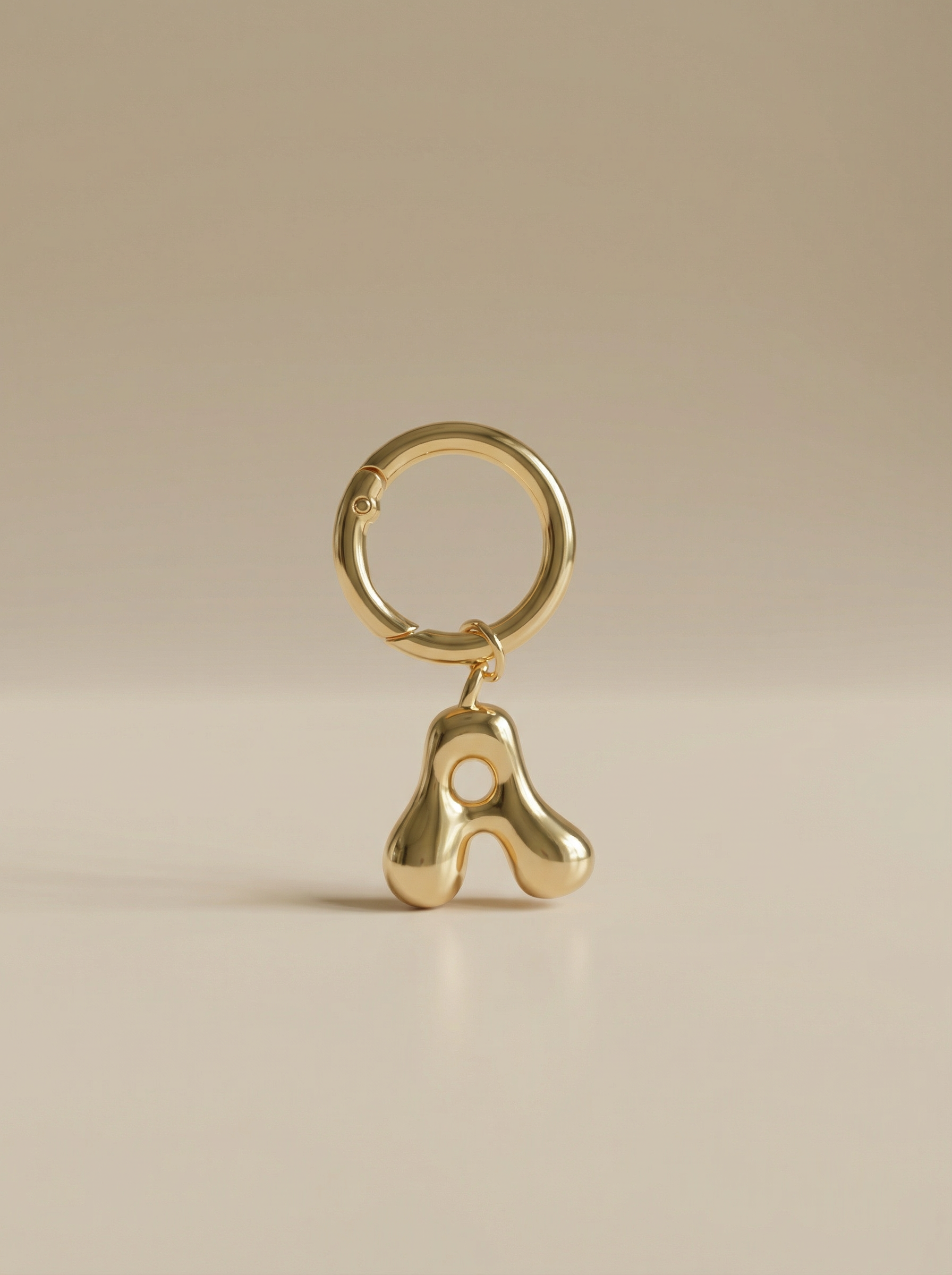 Gold charm in the letter 'A' attached to a gold keyring on beige background