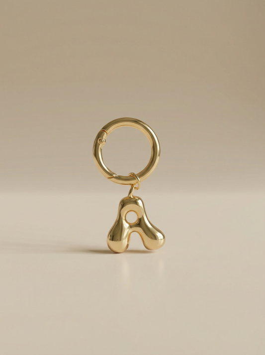 Gold charm in the letter 'A' attached to a gold keyring on beige background