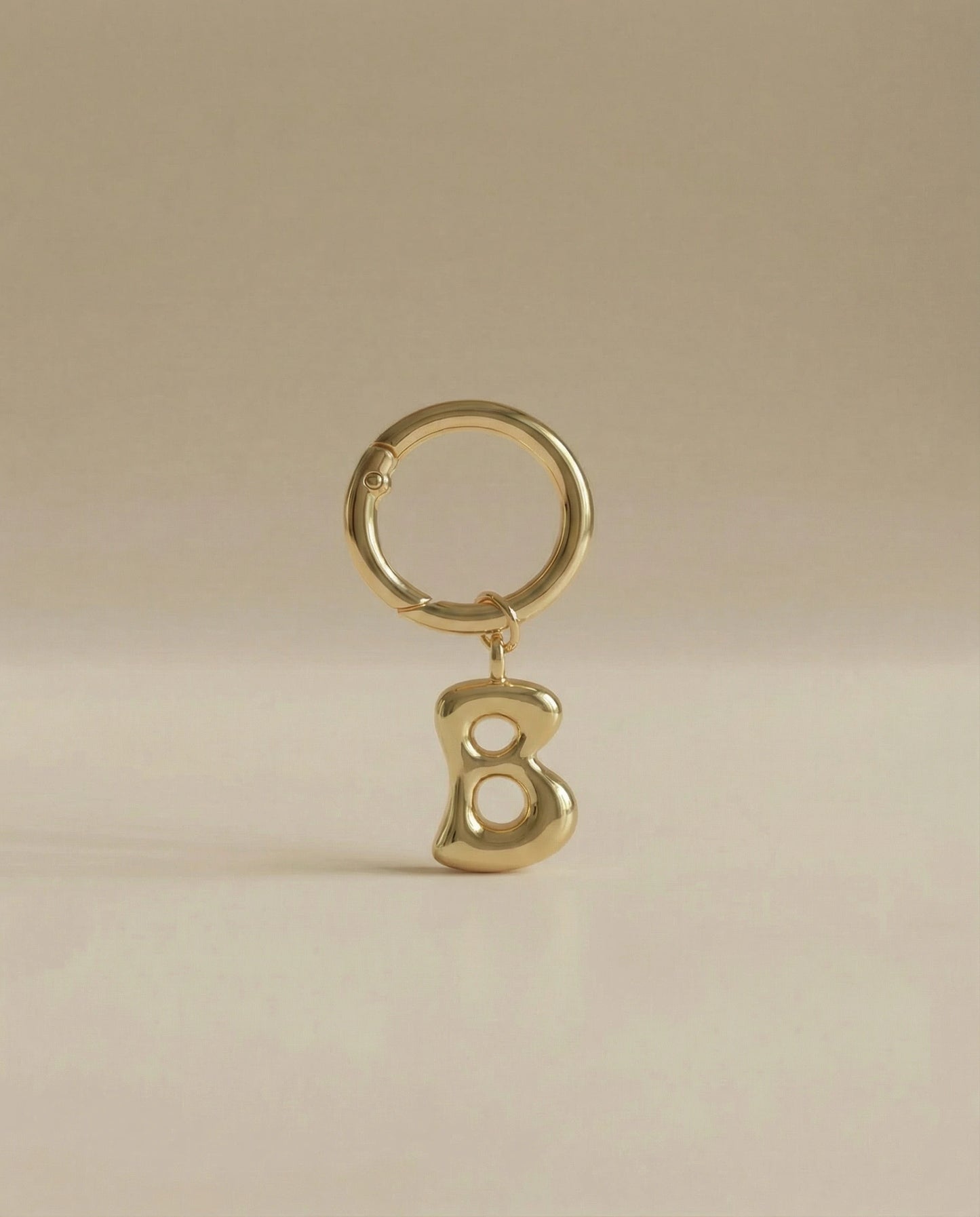 Gold charm in the letter 'B' attached to a gold keyring on beige background