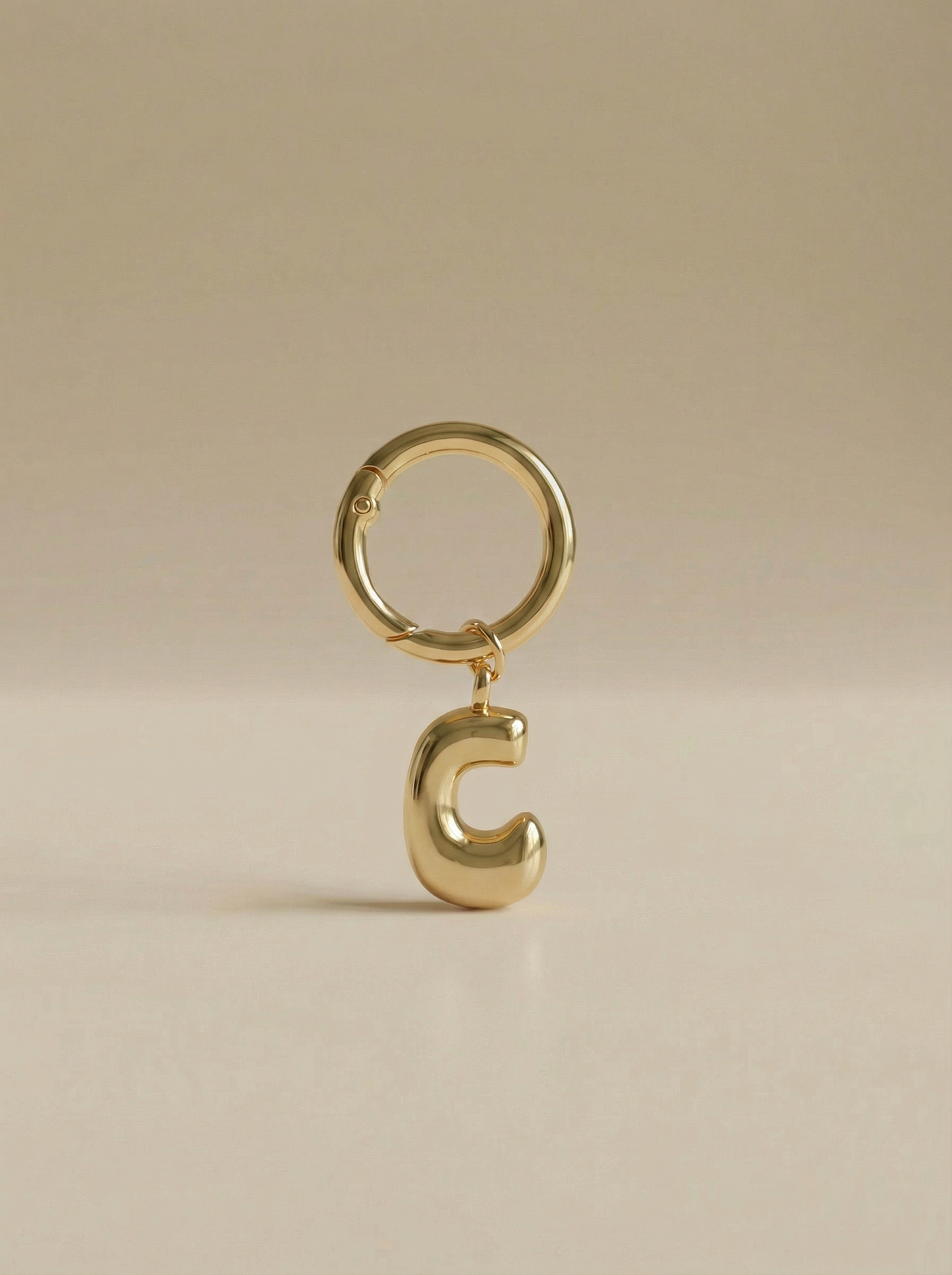 Gold charm in the letter 'C' attached to a gold keyring on beige background