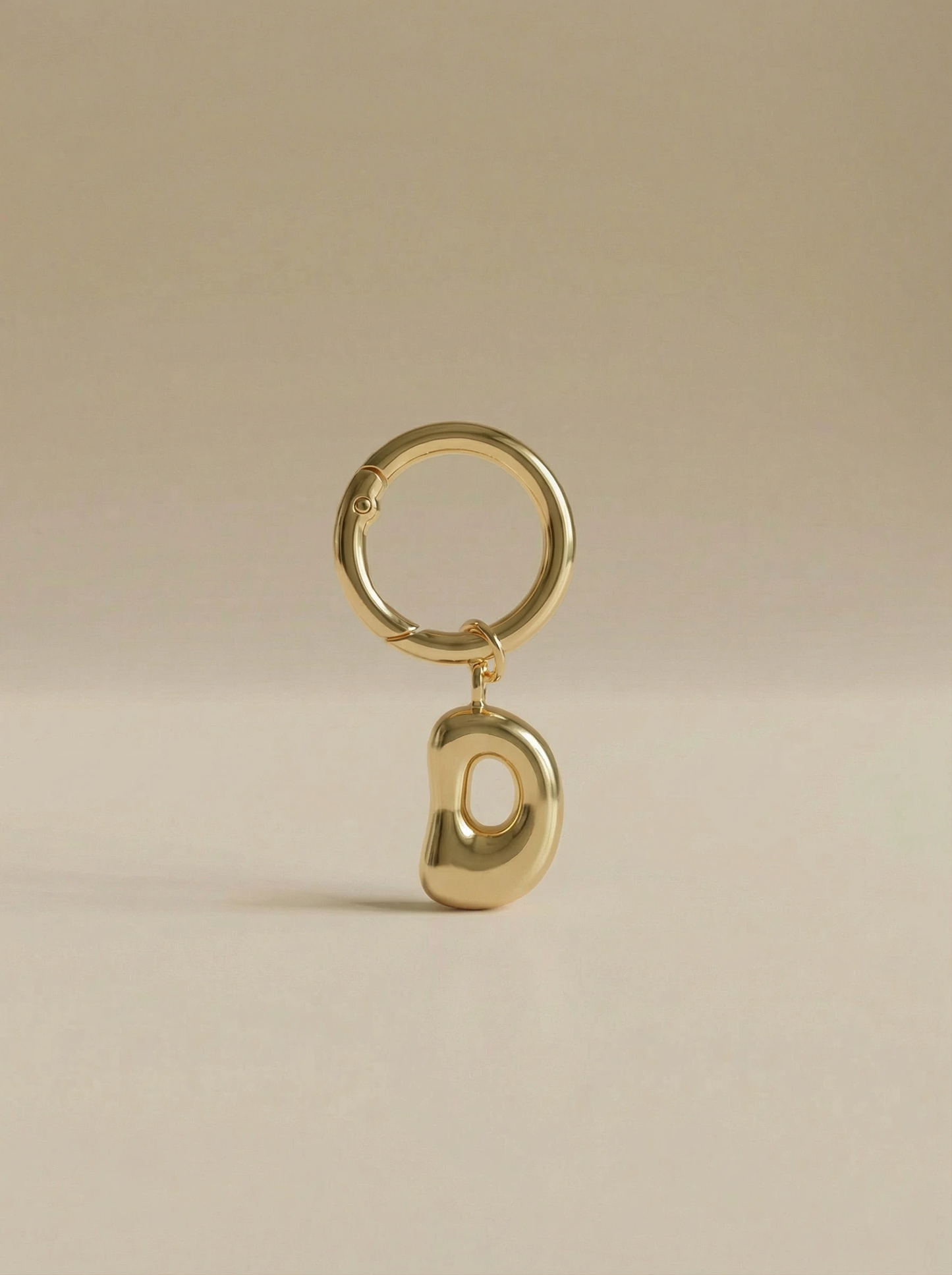 Gold charm in the letter 'D' attached to a gold keyring on beige background