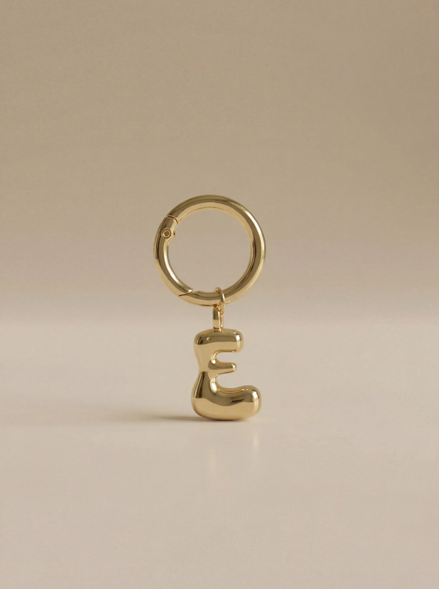 Gold charm in the letter 'E' attached to a gold keyring on beige background