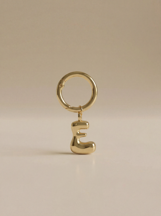 Gold charm in the letter 'E' attached to a gold keyring on beige background