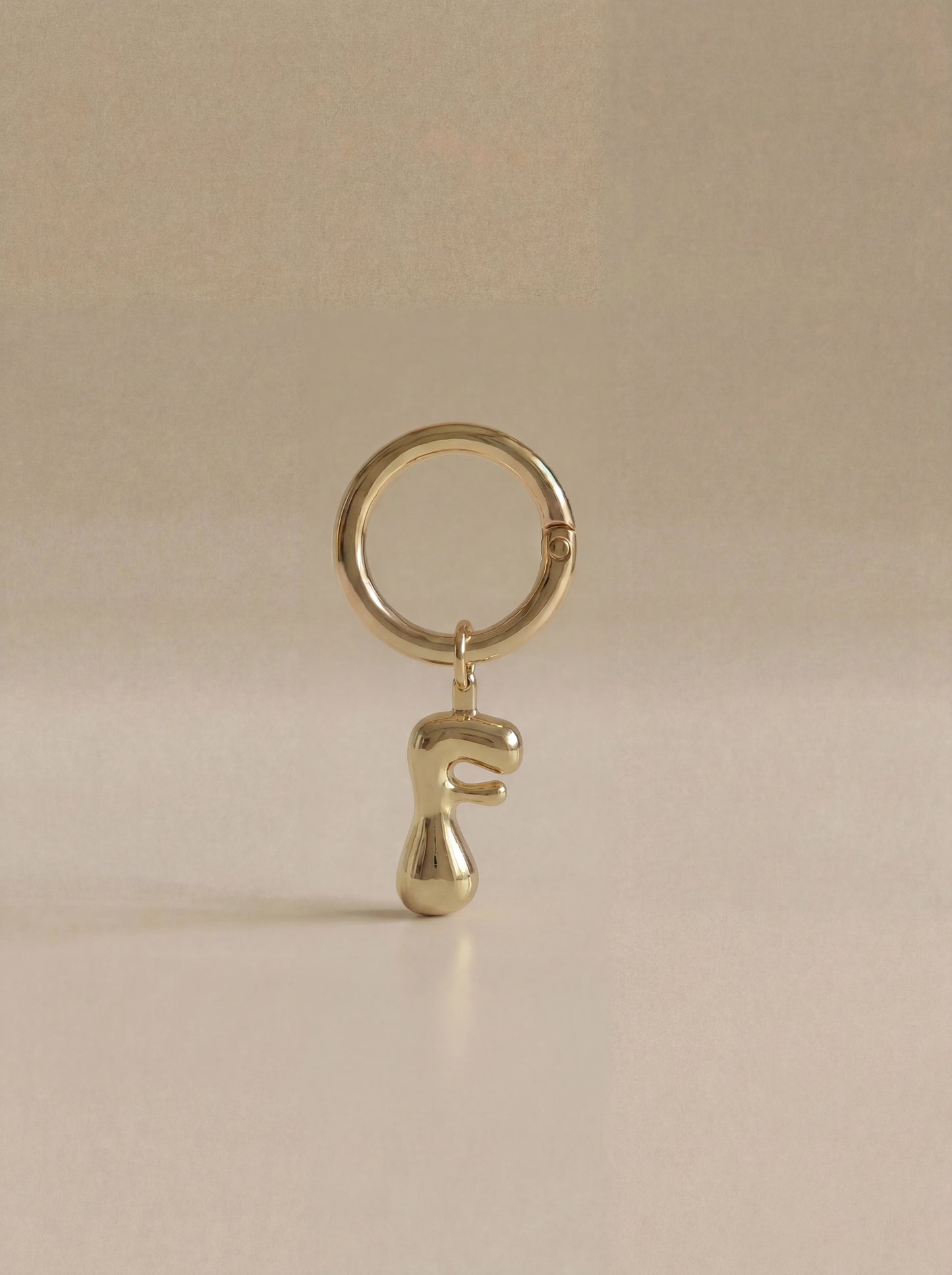 Gold charm in the letter 'F' attached to a gold keyring on beige background