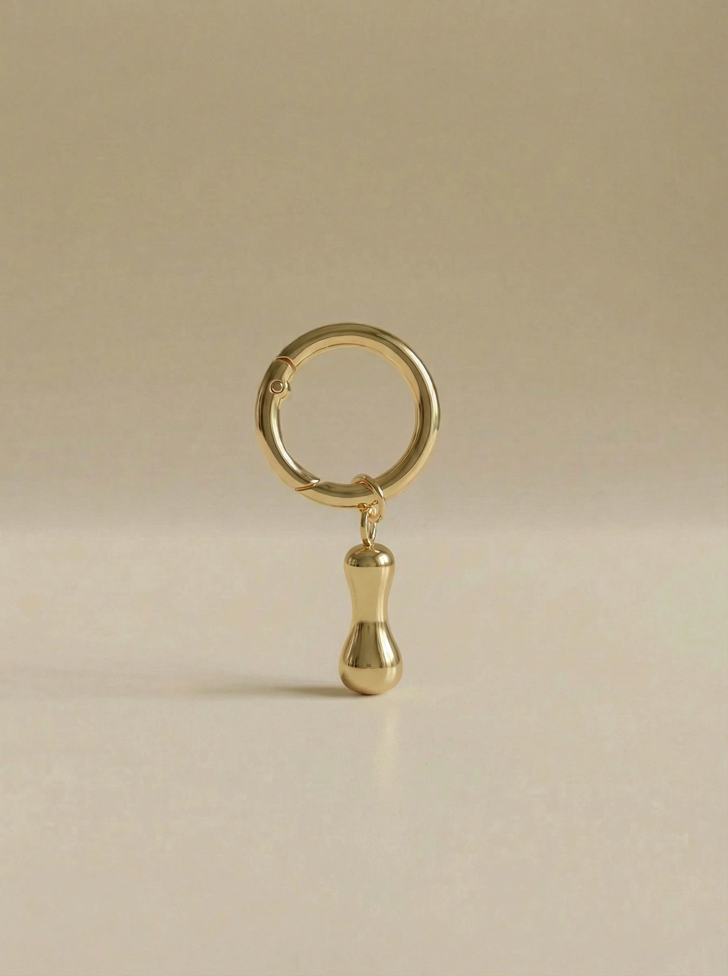 Gold charm in the letter 'I' attached to a gold keyring on beige background