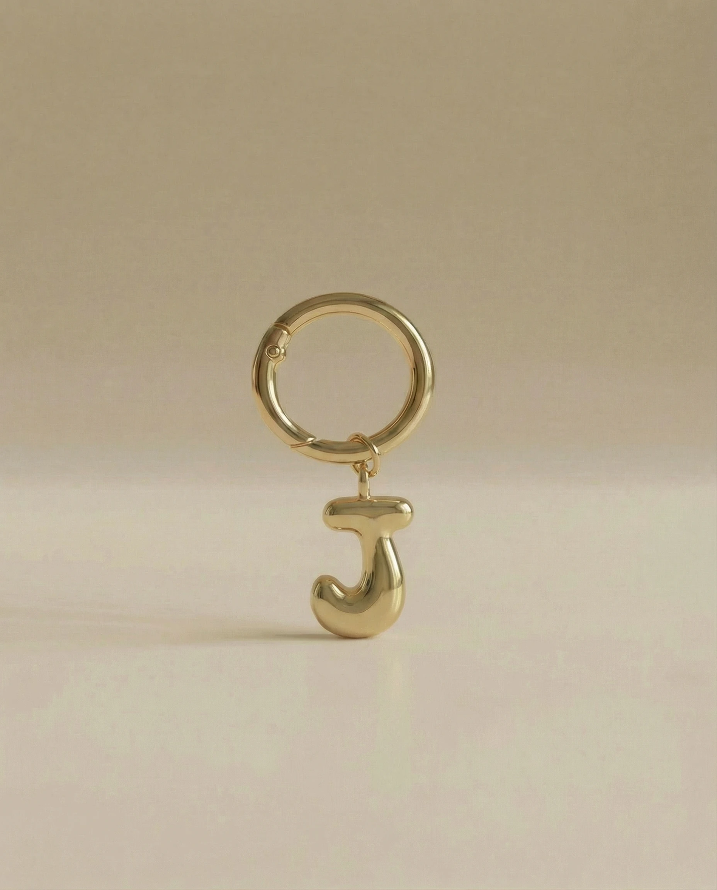 Gold charm in the letter 'J' attached to a gold keyring on beige background