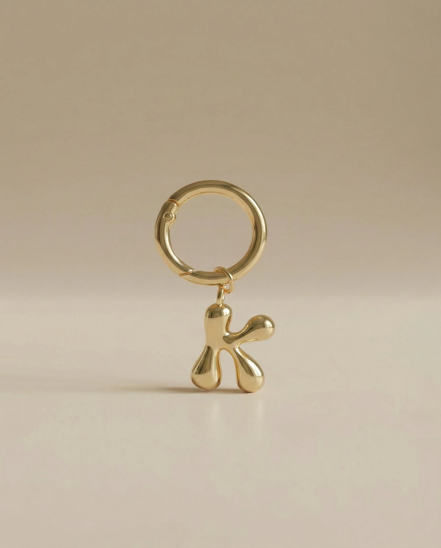 Gold charm in the letter 'K' attached to a gold keyring on beige background