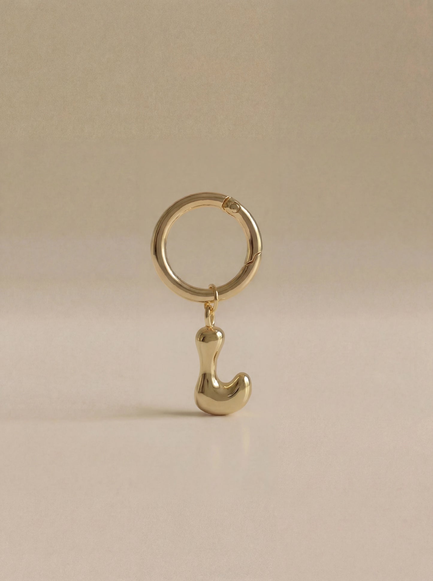 Gold charm in the letter 'L' attached to a gold keyring on beige background
