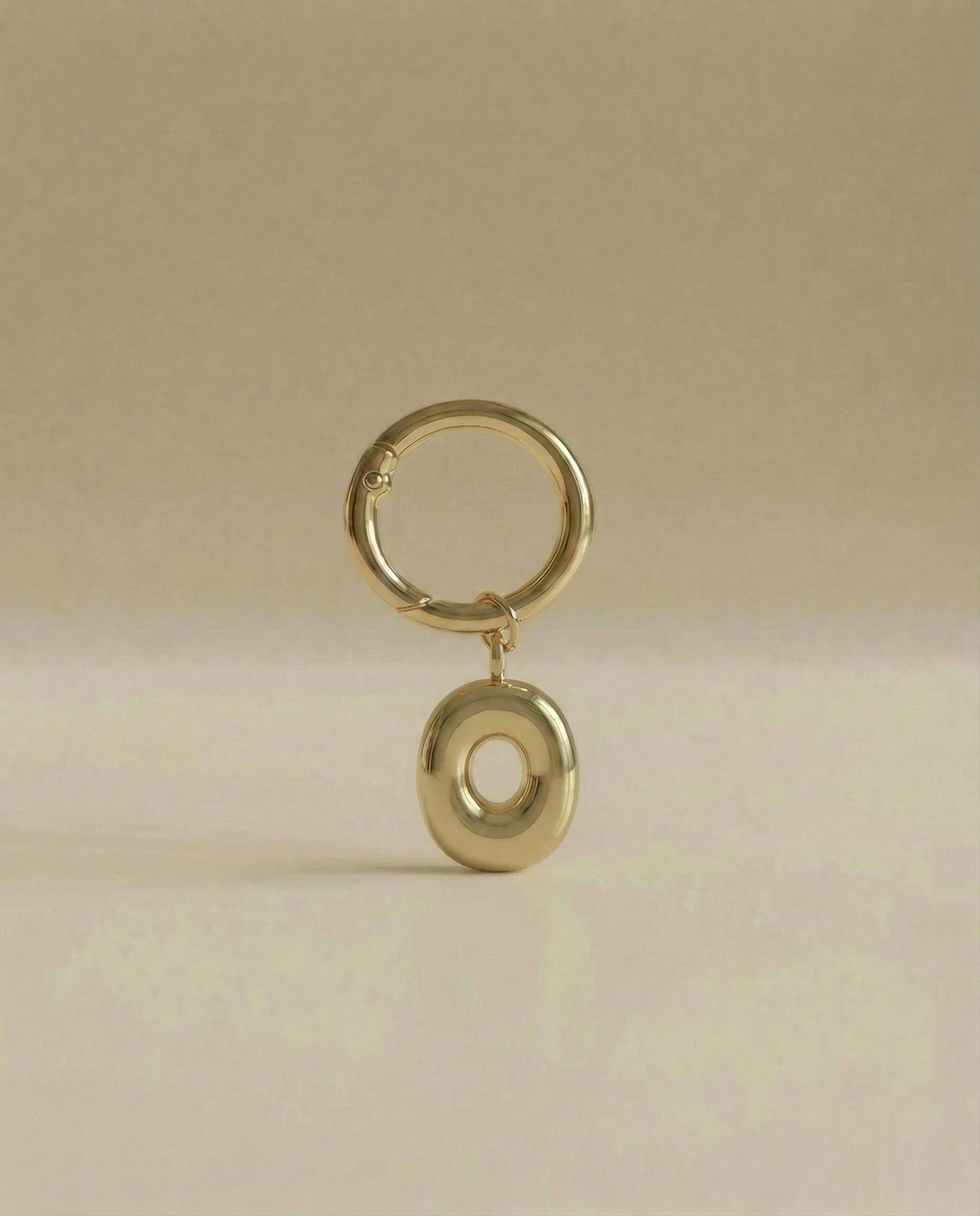 Gold charm in the letter 'O' attached to a gold keyring on beige background