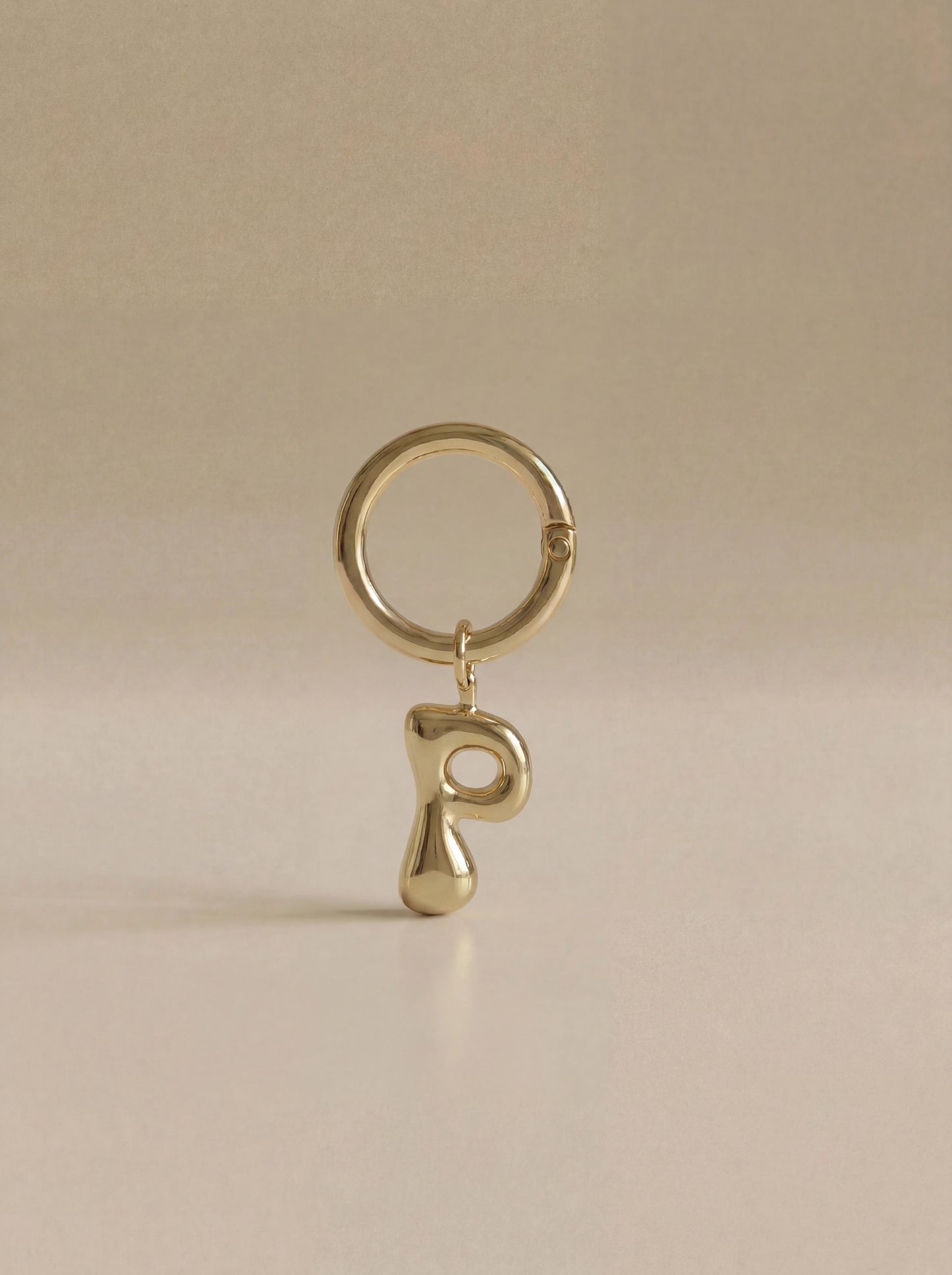 Gold charm in the letter 'P' attached to a gold keyring on beige background