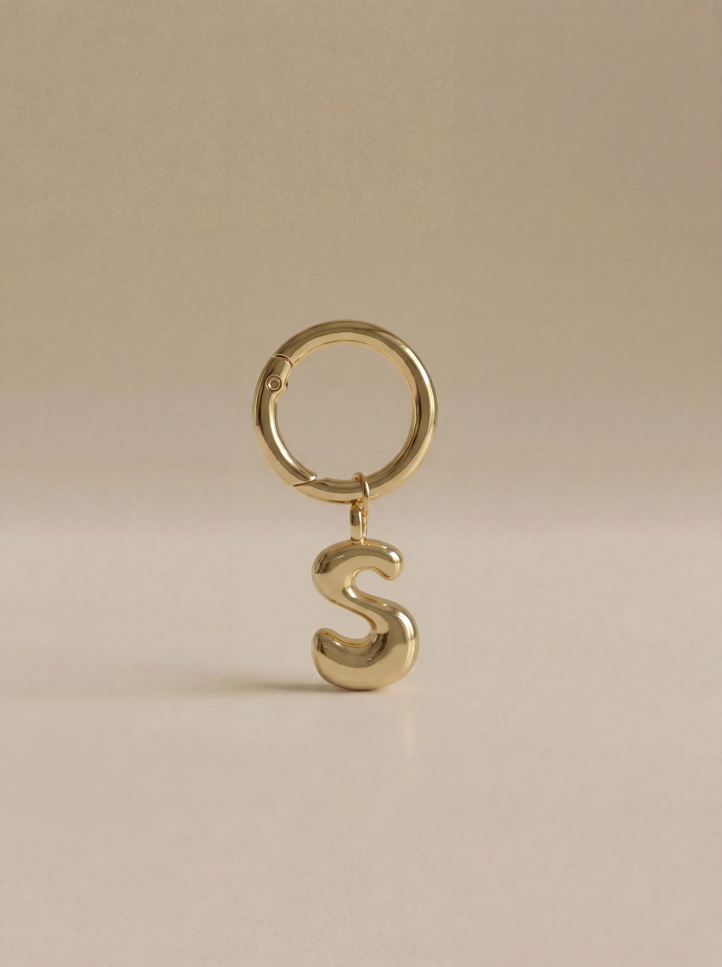 Gold charm in the letter 'S' attached to a gold keyring on beige background