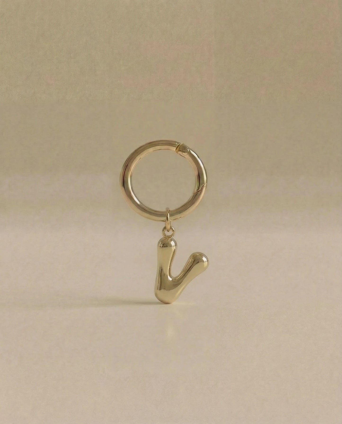 Gold charm in the letter 'V' attached to a gold keyring on beige background