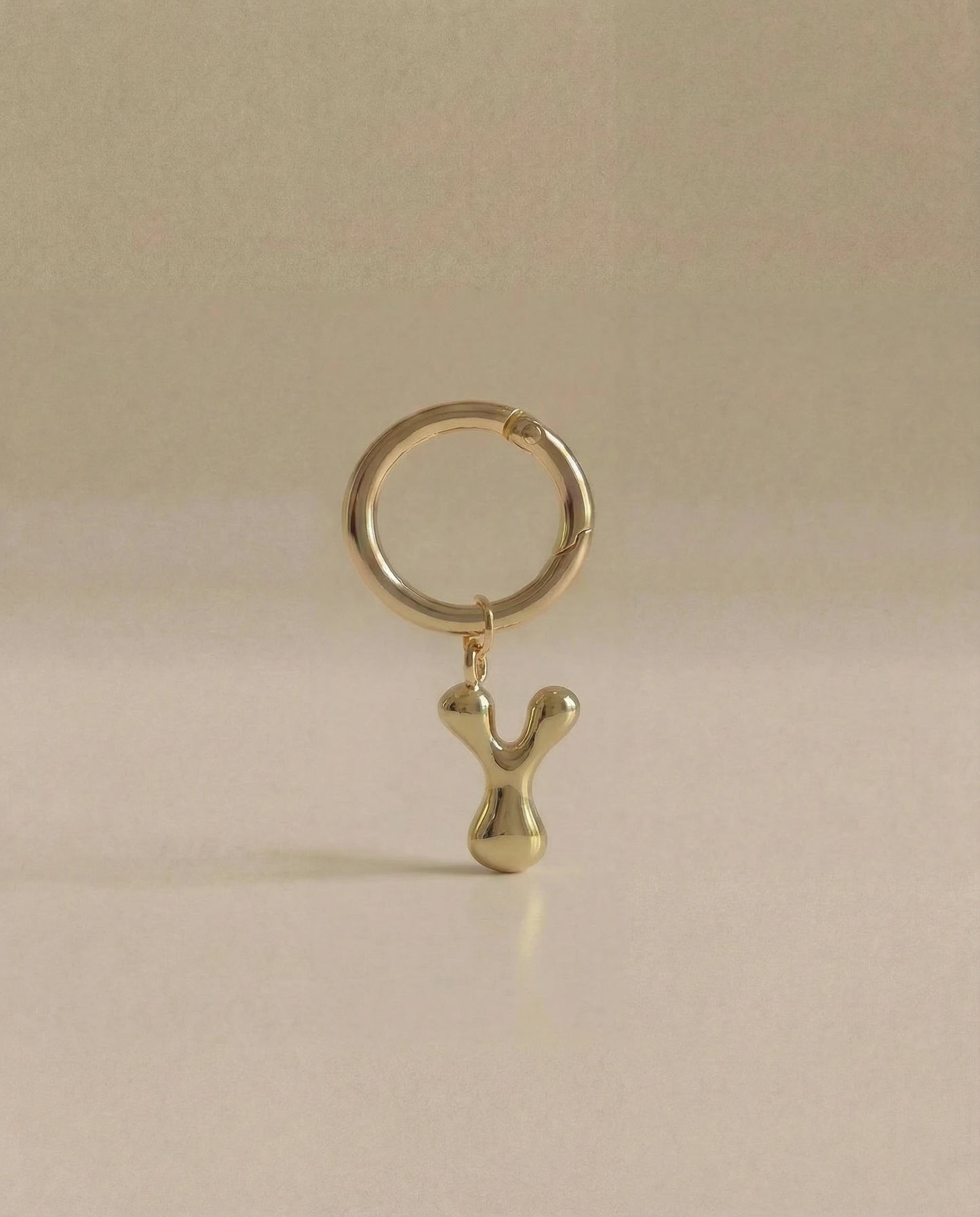 Gold charm in the letter 'Y' attached to a gold keyring on beige background