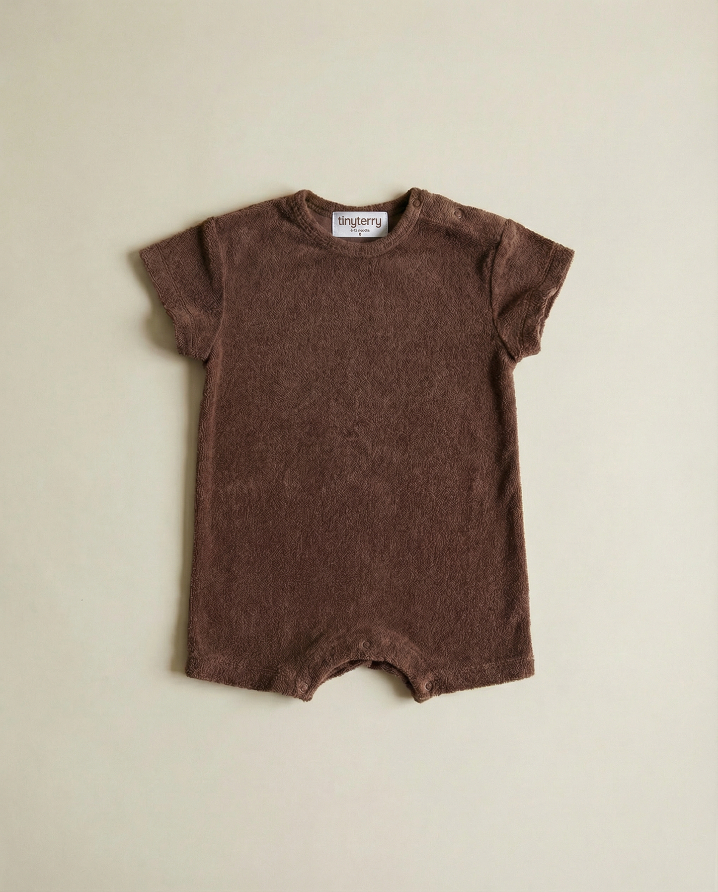 Tiny Terry relaxed terry romper in brown colour flat lay on neutral background on floor in soft natural light 