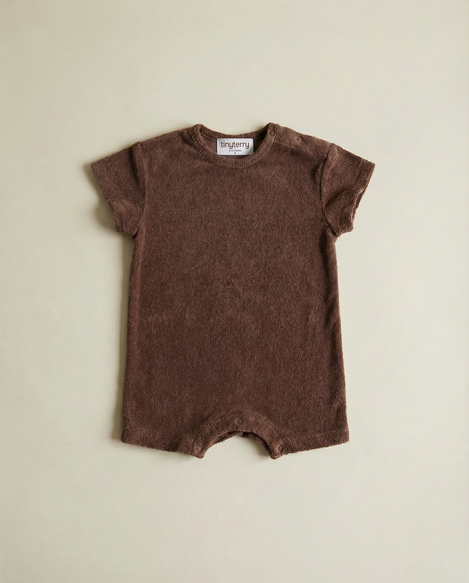 Tiny Terry relaxed terry romper in brown colour flat lay on neutral background on floor in soft natural light 