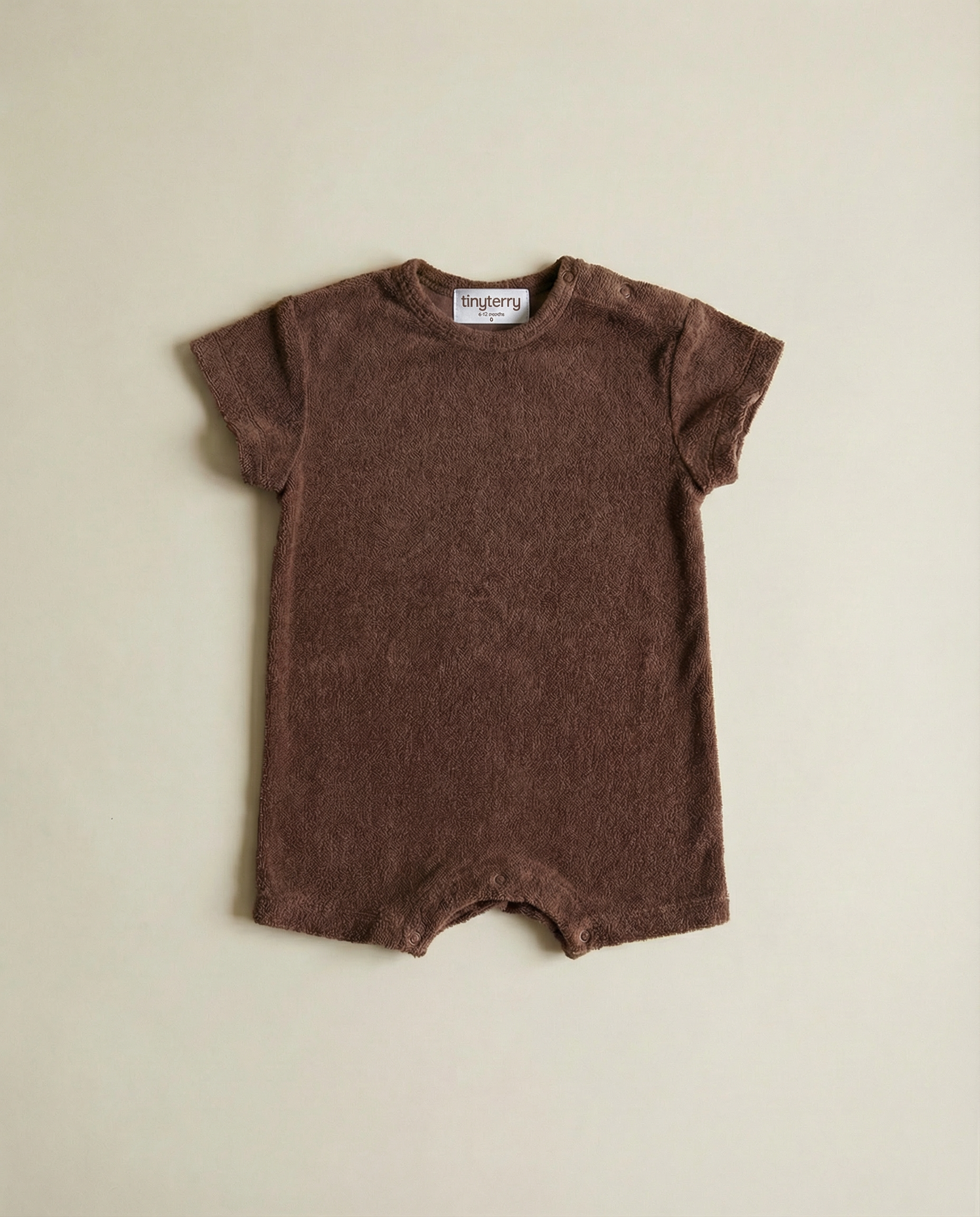 Tiny Terry relaxed terry romper in brown colour flat lay on neutral background on floor in soft natural light 