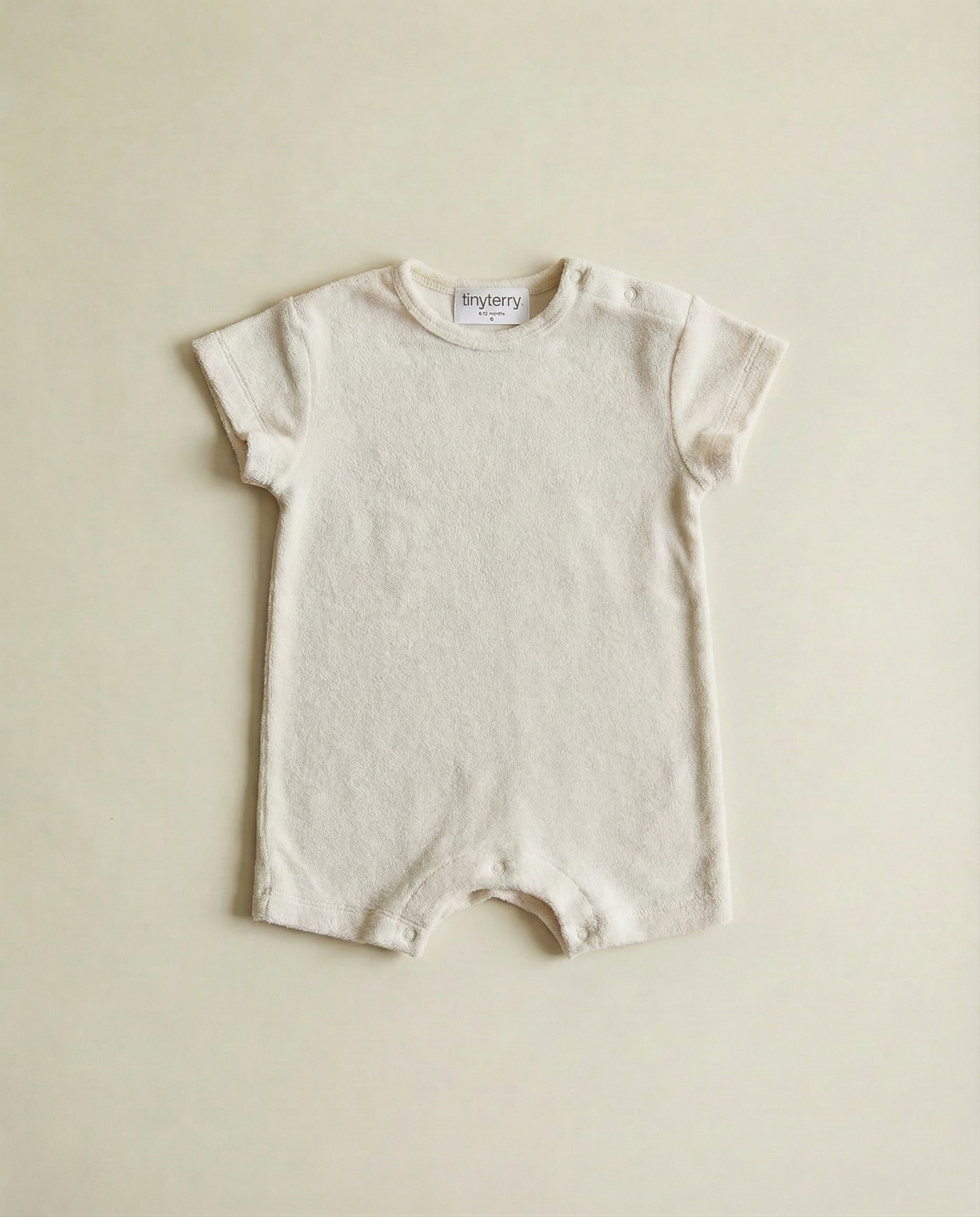 Tiny Terry relaxed terry romper flat lay on neutral background on floor in soft natural light 
